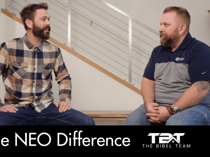 Eric Bibel and Brad Soll are seated in chairs in front of an aluminum stair rail and a white wall.